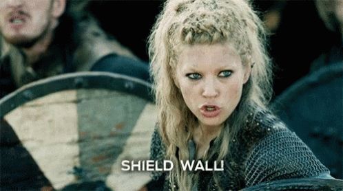 Szene aus der Fensehserie Vikings in der eine weibliche Wikingerin "Shied Wall" ruft und darauf hin eine Reihe Wikinger ihre Schilde aufstellen.