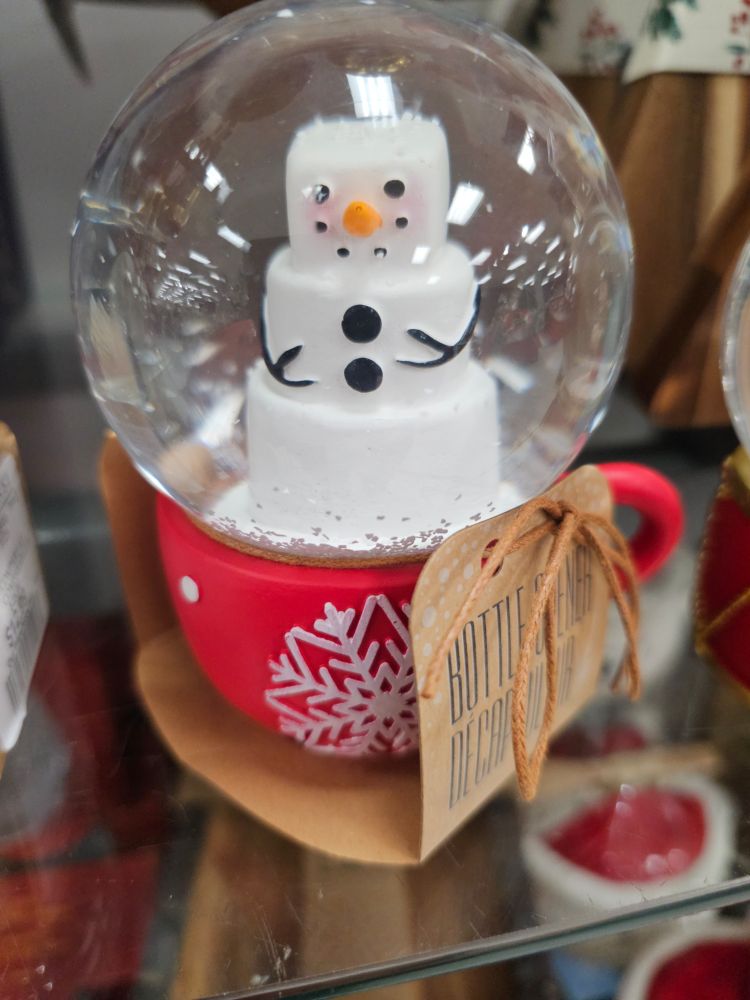 A small snow globe with a base shaped like a mug and a marshmallow show man in the globe part
