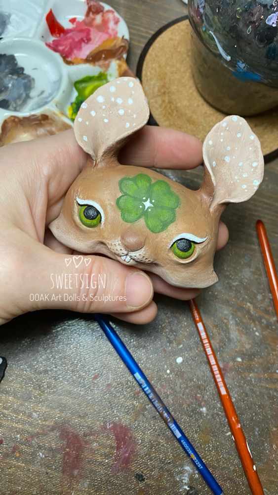 Beige rabbit’s head with a green clover leaf on its forehead, handmade original art doll in progress by Svetlana Polupanova 