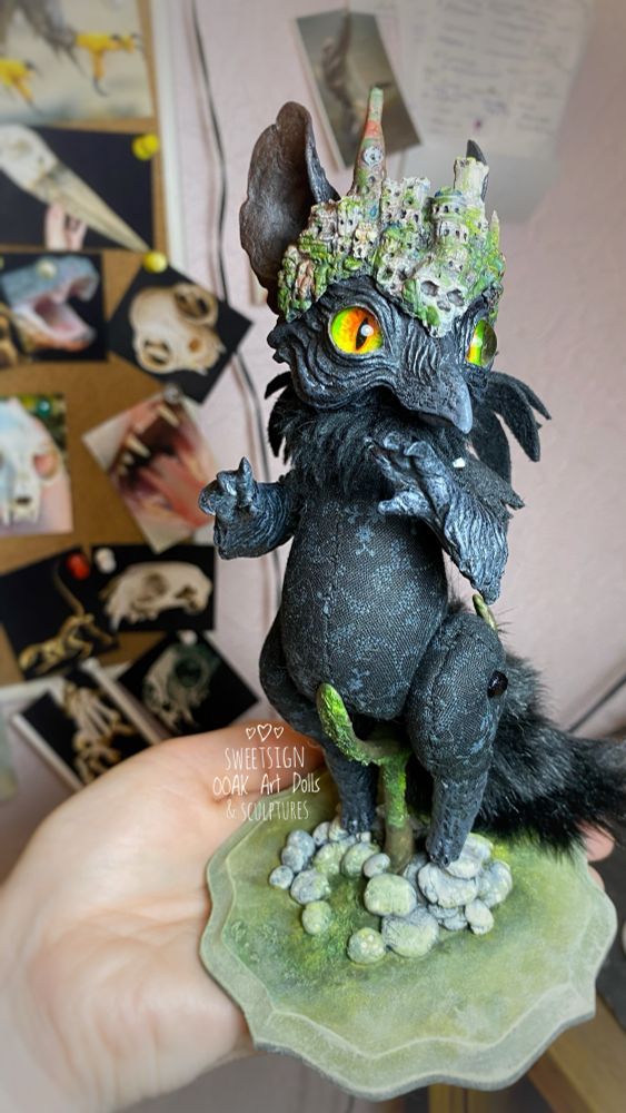 An original miniature fantasy art doll in progress, black raven griffin with a city remnants as its headdress. It is placed on an especial stand I made for it, all sculpted and painted manually. 