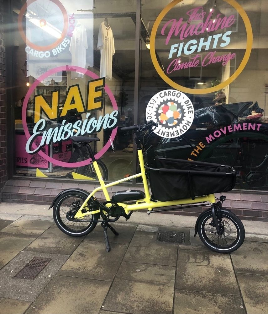 A yellow front loading 'Yoonit' cargo bike, parked on the pavement in front of the Cargo Bike movement HQ in Edinburgh