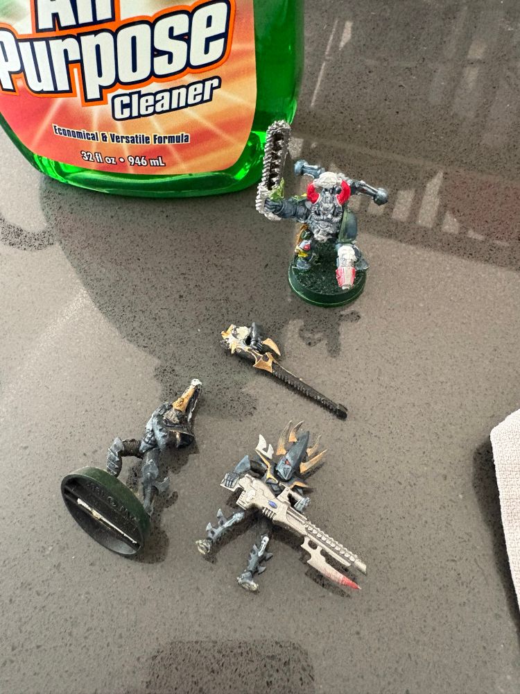 The chaos champion mini, along with two dark eldar warriors, displayed next to a bottle of Simple Green cleaner.