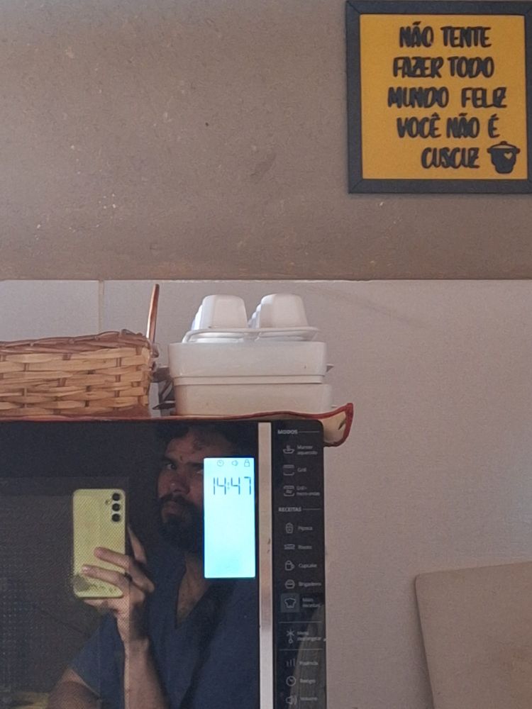 Foto com um microondas mostrando a hora 14:47 e um quadro escrito "Não rente fazer todo mundo feliz você não é cuscuz"