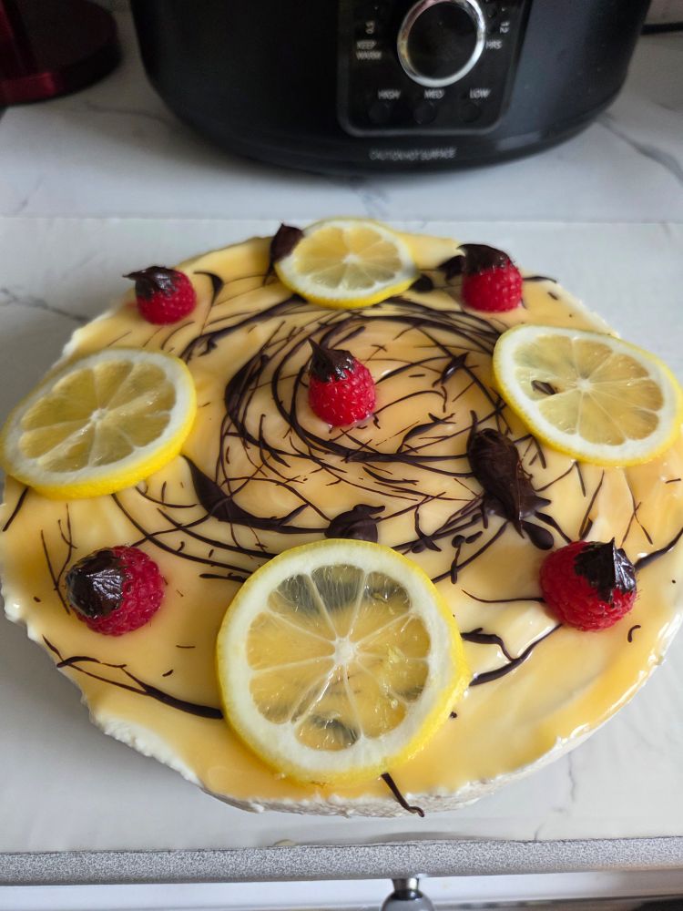 A no-bake lemon curd cheesecake decorated with sliced lemon, chocolate drizzle, and chocolate dipped raspberries.