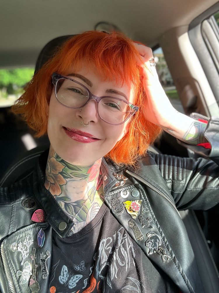 A picture of Stina with a jacket with a ton of enamel pins. Her hair is a big orange mess. 
