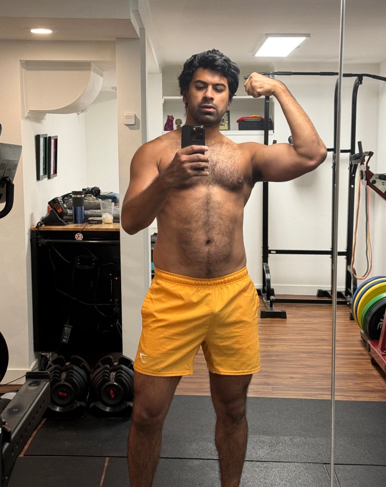 shirtless mirror gym selfie flexing a bicep pump. wearing bright orange gym shorts. 