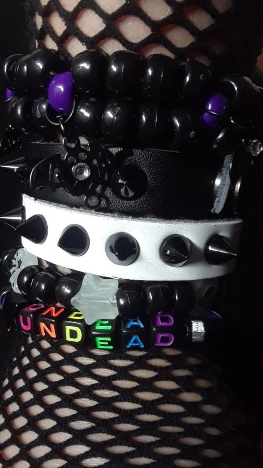 Someone's arm with fishnets stacked spiked bracelet and goth Kandy. Rainbow and black beads that say "undead" 