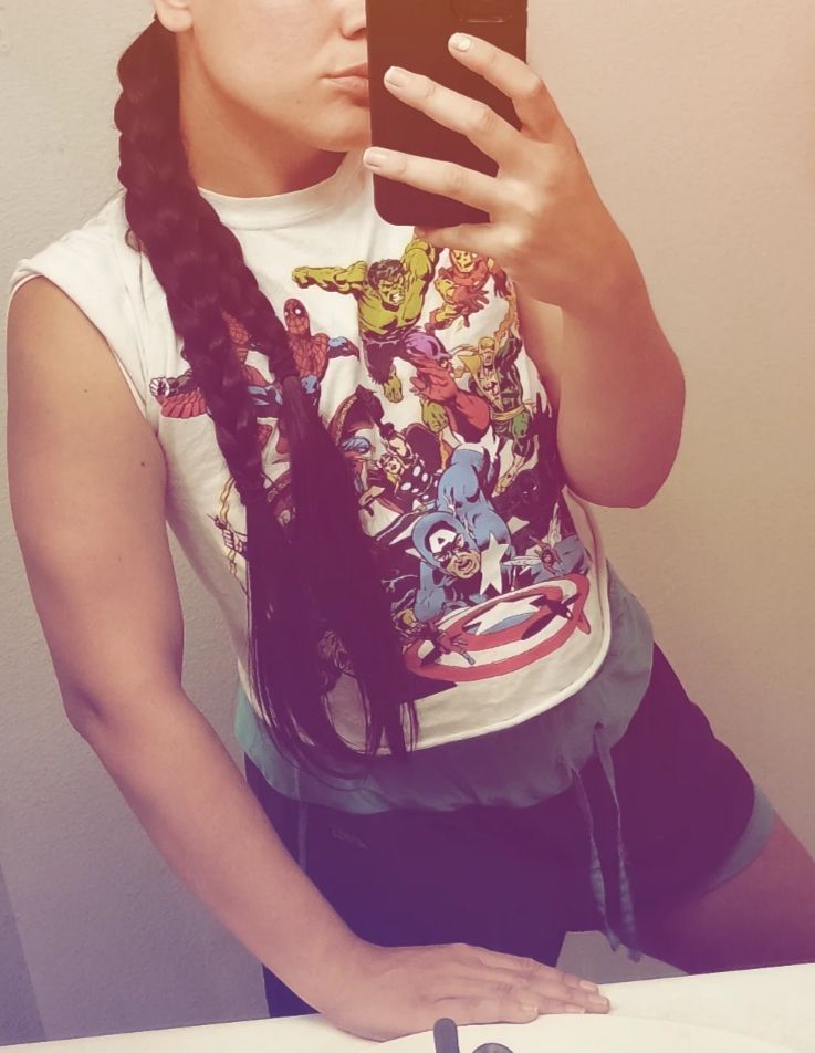 Bathroom Mirror selfie with my face cropped out. Wearing a crop top comic marvel shirt and some green track shorts with an purpley orange ig filter. showing off my arm toning progress.  