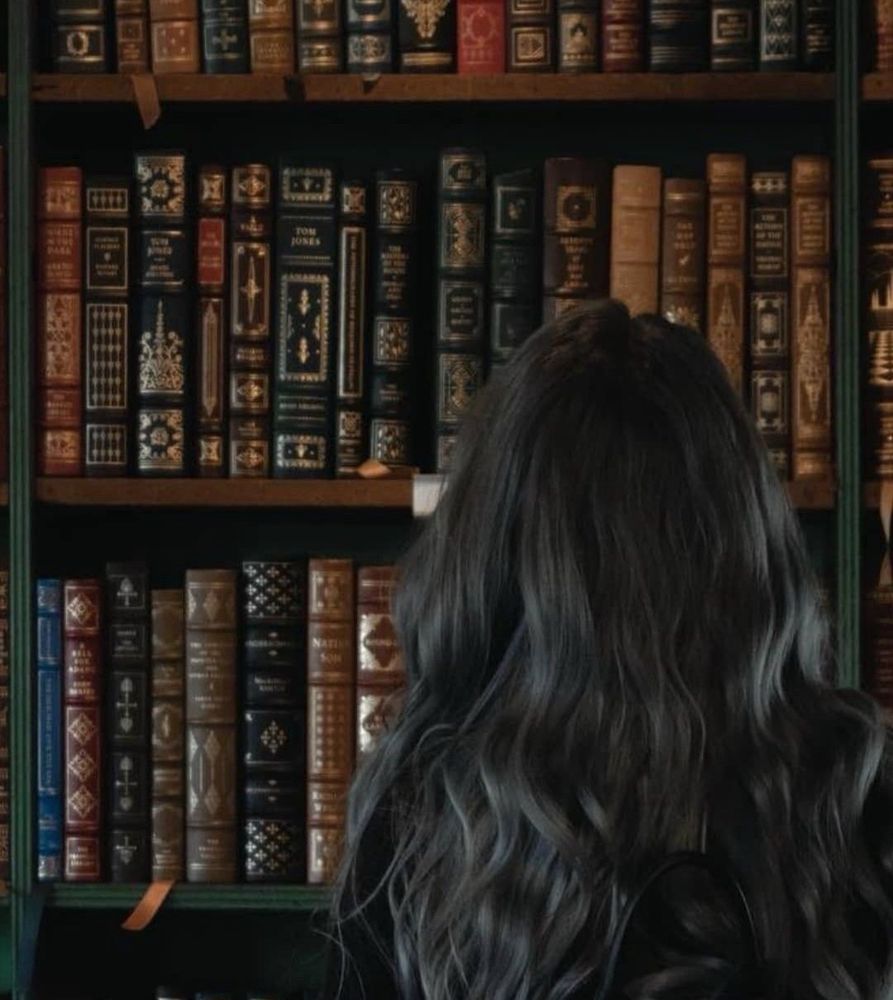 Person with long hair looking up at rows of books with a variety of different spines 