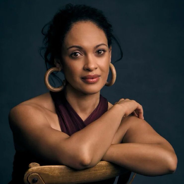 Cynthia in still from Swagger Magazine photoshoot. She’s sitting backwards in a wooden chair, with her arms folded over the chair back, looking gorgeous as usual.