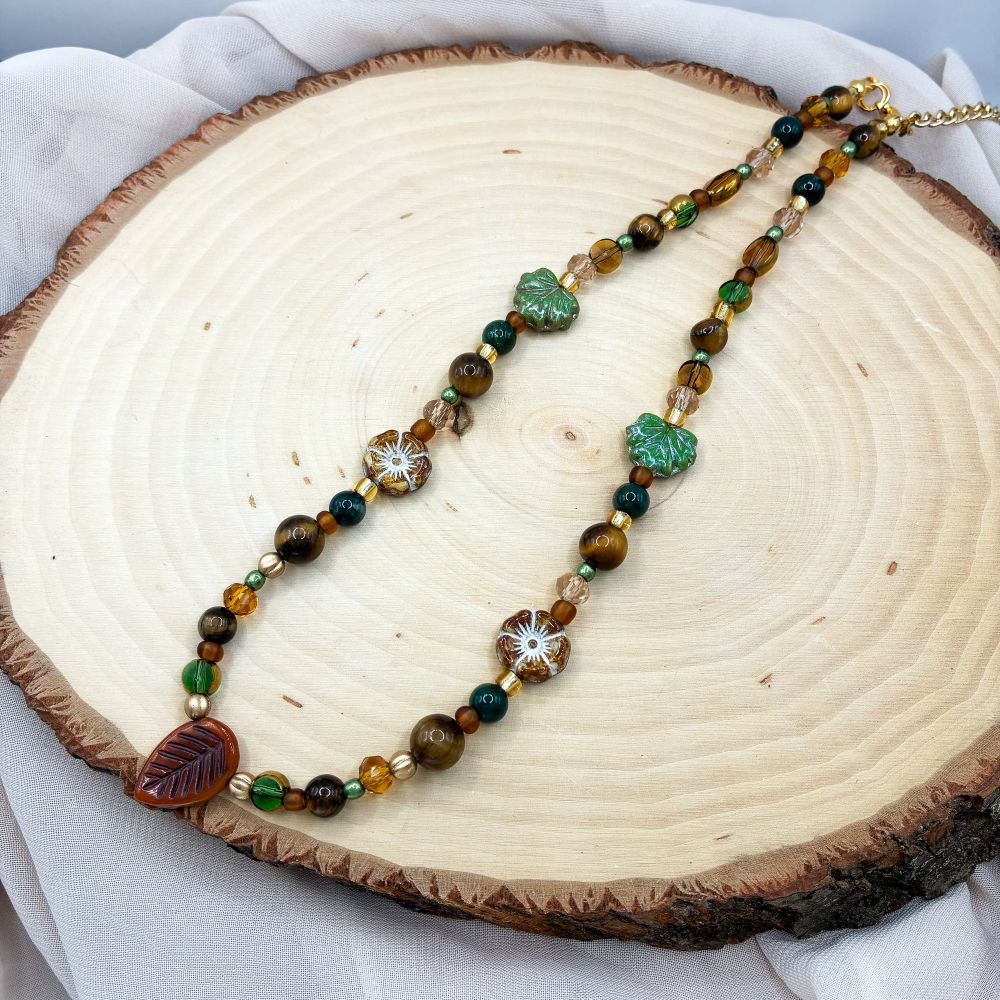 A fall themed necklace with a brown leaf pendant, and a variety of earth toned beads 