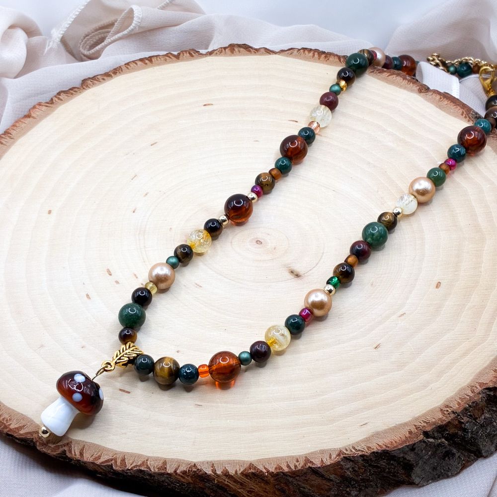 A beaded necklace with a mushroom pendant. The beads are moss agate, tigers eye, heat treated amethyst (“citrine”) and a variety of glass beads 