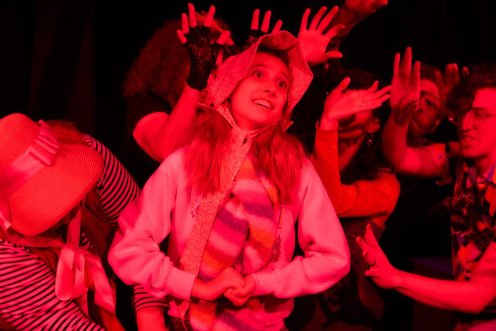Improv show of a main character in awe surrounded by other characters in a fan shape. Lighting is in red.