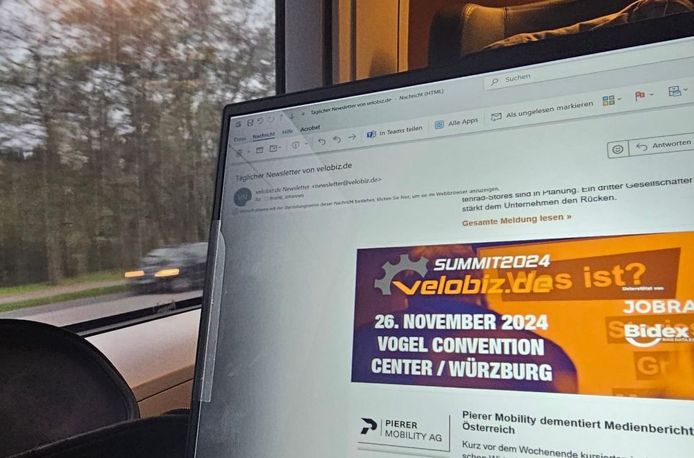 Laptop-Bild mit Einladungs-Mail Velobiz Summit und Landschaft im Hintergrund aus dem Zugabteil.