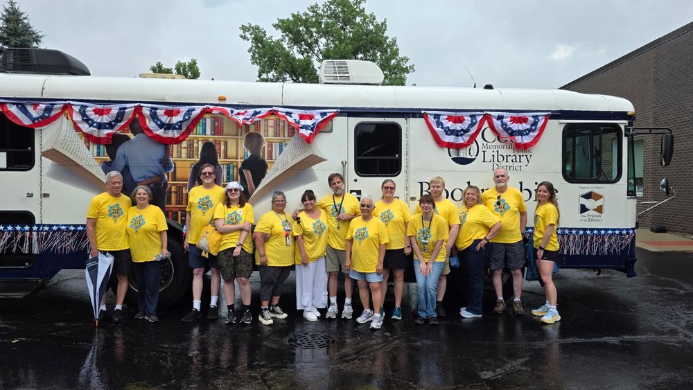 Staff members posing in front of the Bookmobile in the rain before the Vernon Hills Fourth of July parade.
