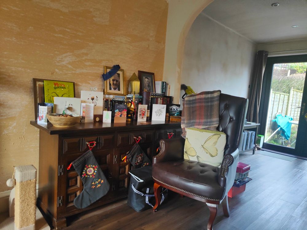 A dark wood sideboard adorned with Christmas cards.  A brown chesterfield-style chair stands nearby
