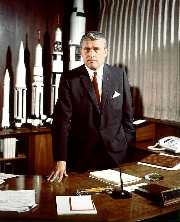 Werner von Braun in seinem Büro in den 1960er Jahren. Hinter ihm Modelle der Raketen die er entwarf, ganz rechts die Saturn V des Apollo Programms der NASA.