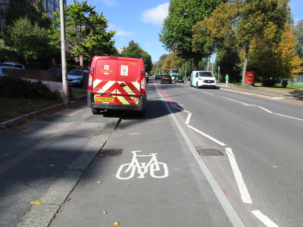 Rear view of a post van parked half on pavement and half on cycle lane.