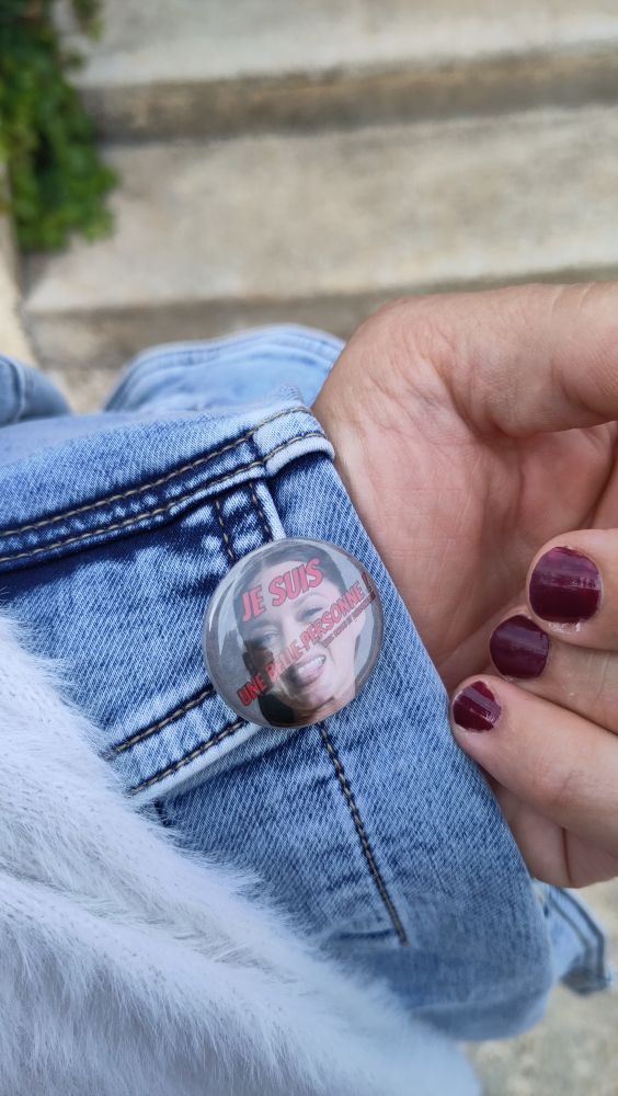 Sur une veste en jeans portée sur le bras, un badge "je suis une belle personne" avec la photo de Marion Cotillard qui tire la langue en fond. 