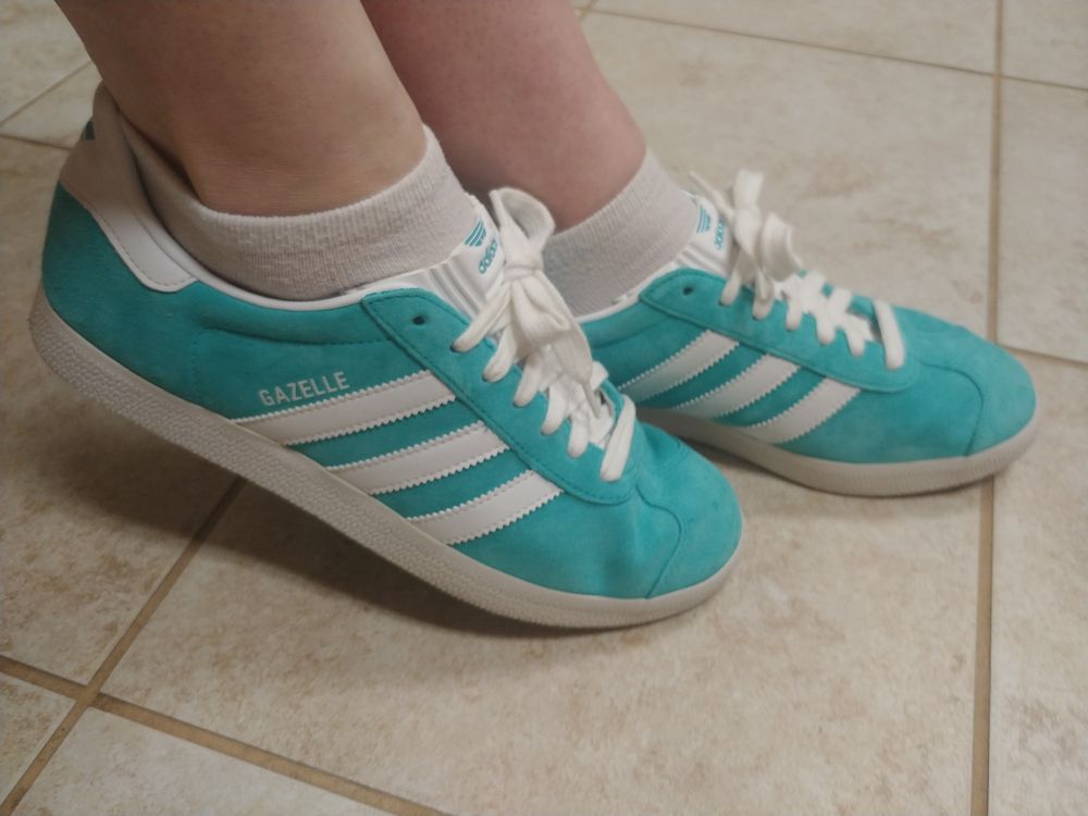 A pair of turquoise Adidas sneakers, posing coyly in their native habitat.
