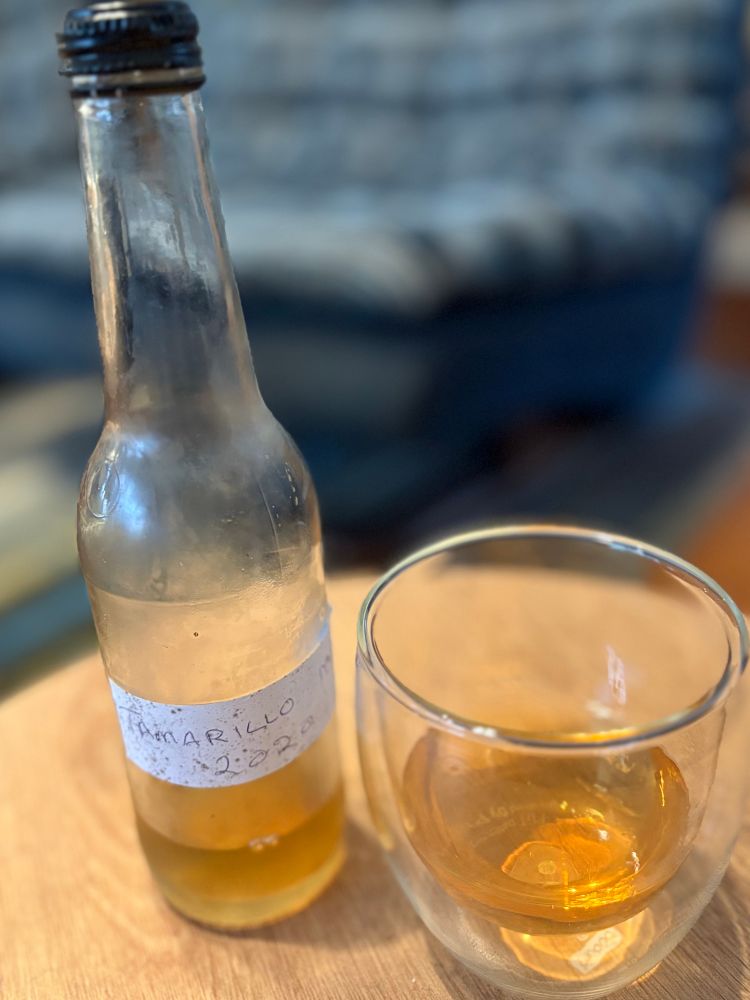 A small grubby glass bottle of golden liquid, only quarter full with Tamarillo 2020 written on it, next to a glass with the same liquid in it. 