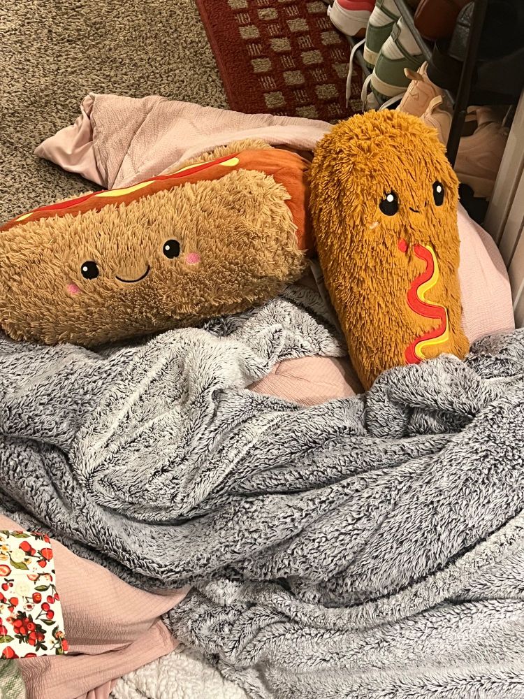 A large stuffed smiling hot dog and corn dog nestled in soft blankets