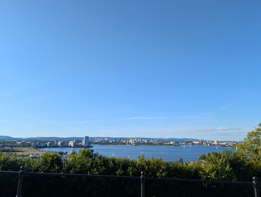 View of Cardiff bay. It's sunny with no clouds. There's tower blocks in the background and water in the foreground 