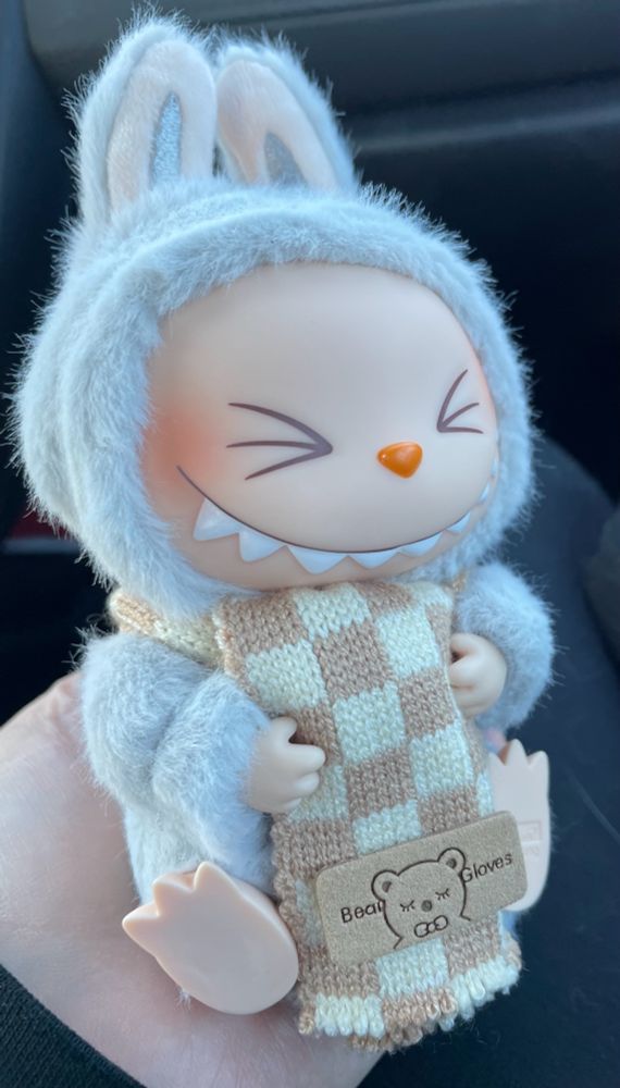 A picture of the Labubu plush, Hehe, in a cute cream and tan checkered scarf.