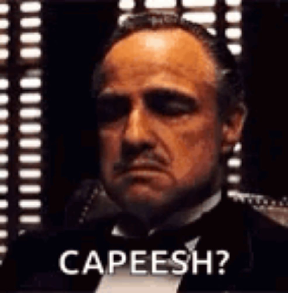 a man in a tuxedo is sitting in front of a window and says `` capeesh '' .