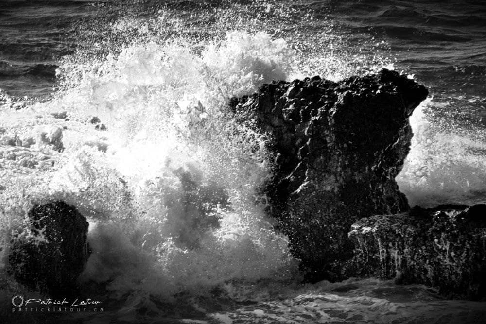A black and white photo of a wave crashing on some rocks