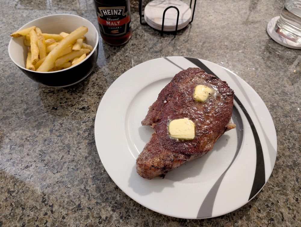 The ribeye steak, post-searing, served with a couple pads of extra butter and some fries on the side.