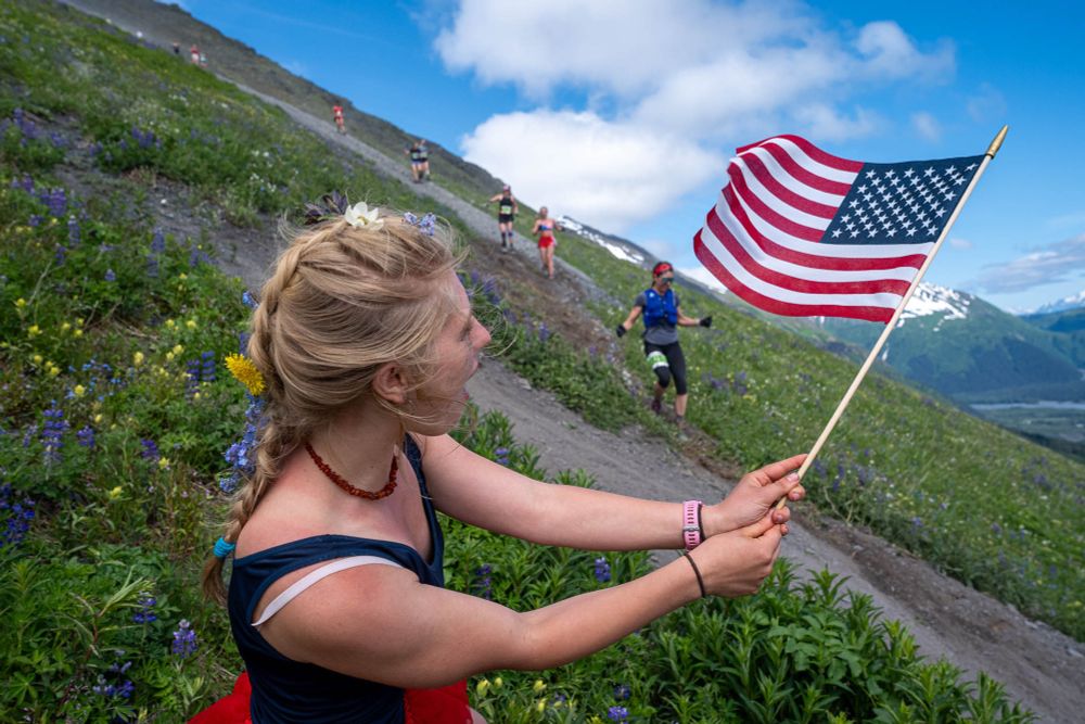 Riga Grubis waves a flag as she cheers on competitors in the 97th running of the Mount Marathon race on Friday, July 4, 2025 in Seward.
