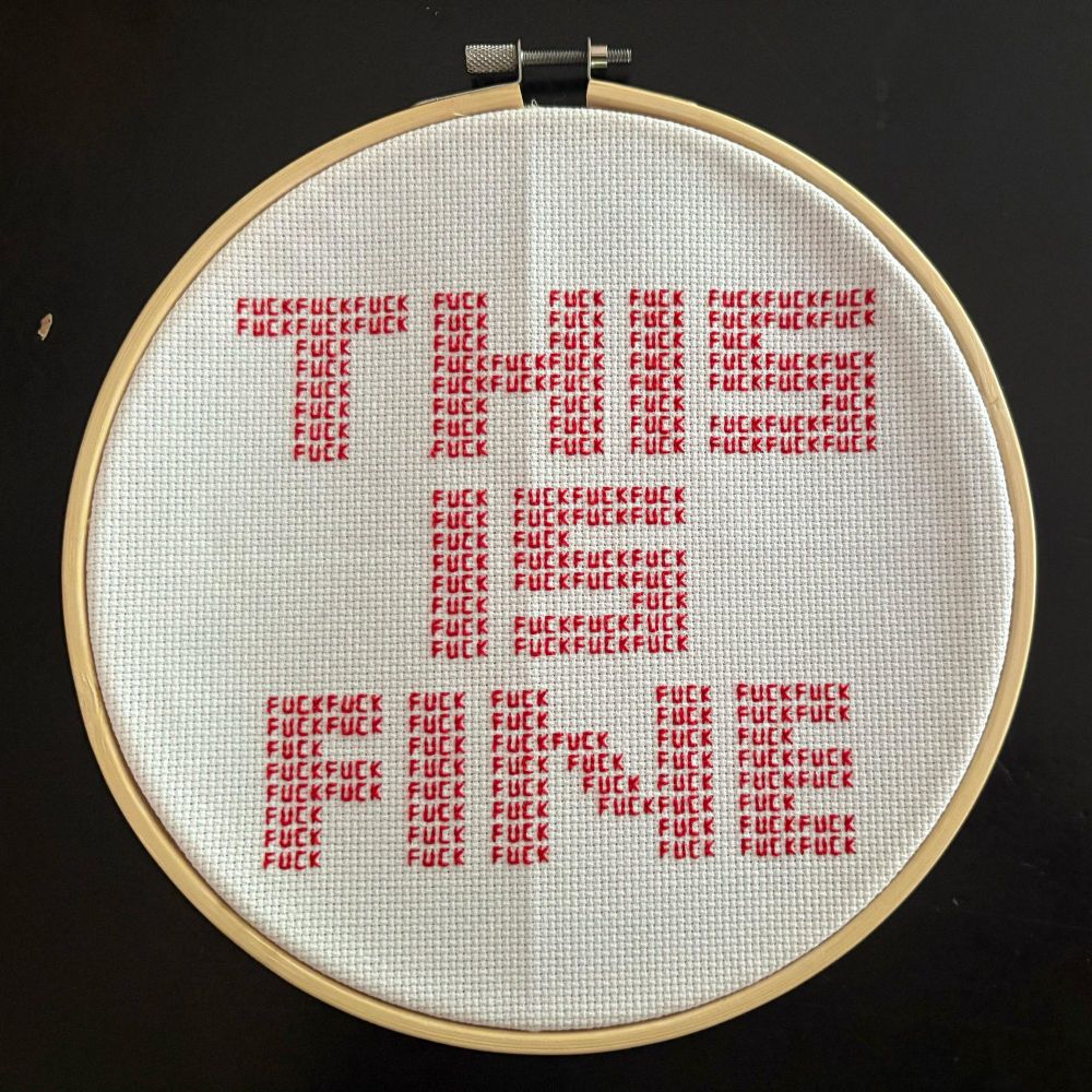 Embroidery with the text "THIS IS FINE". When you zoom in, you see the letters are made up of a lot of tiny words: FUCK.
