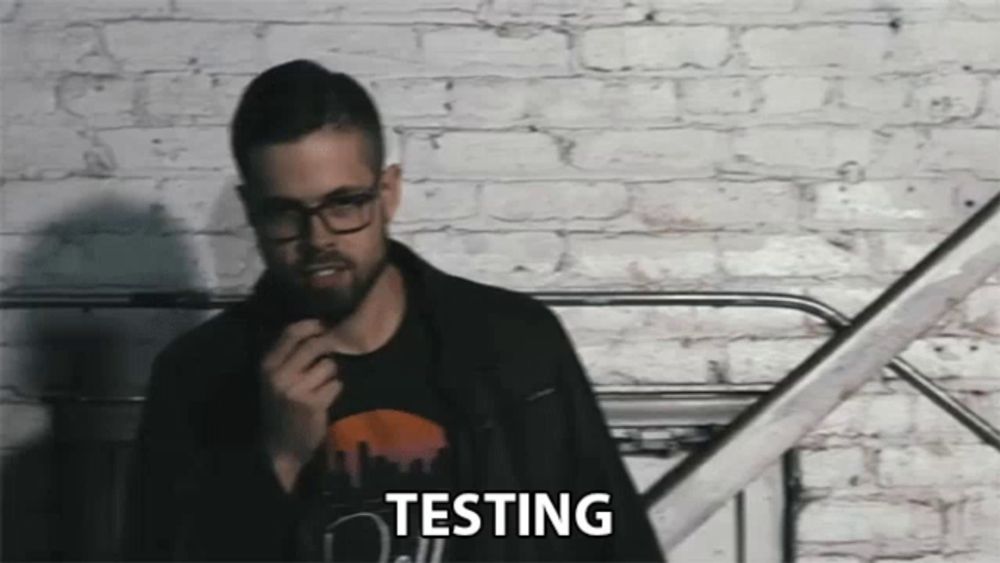 a man standing in front of a white brick wall with the word testing on his chest