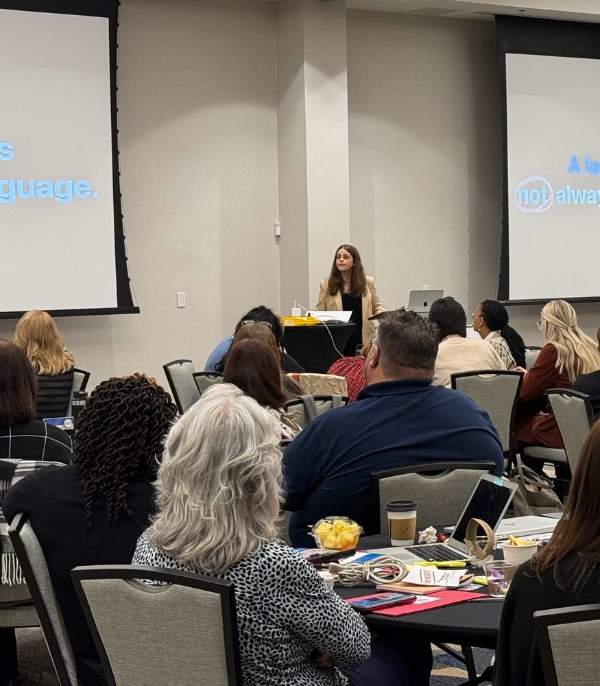 Jordyn, standing at the front of a crowded ballroom full of attendees, presenting. There are screens on both sides of her.