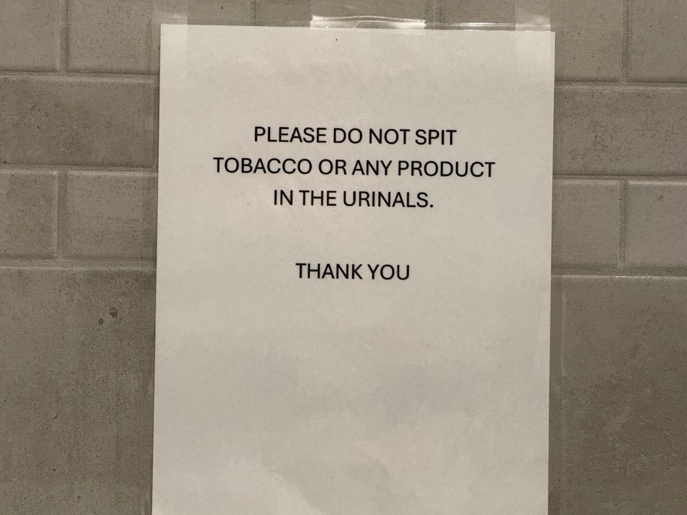 An enlarged version of a paper between two urinals with the message “Please do not spit tobacco or any product in the urinals. Thank you.”