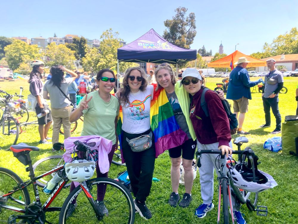 Big smiles from 4 riders decked out in rainbows at the end of the ride. More people hanging out in the back on a beautiful sunny day.