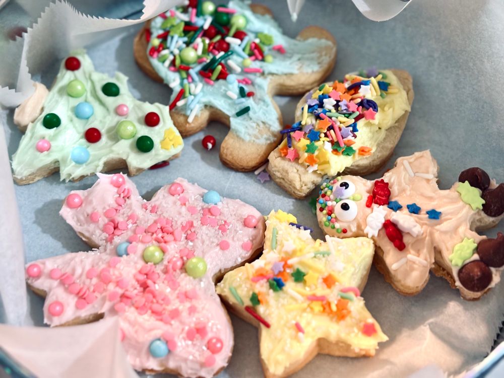 Some decorated sugar cookies. A star with yellow icing & sprinkles, a pink bow with pearl candies & sprinkles, a christmas tree with pearl candies for ornaments, a gingerbread man, a christmas light and another gingerbread man.  