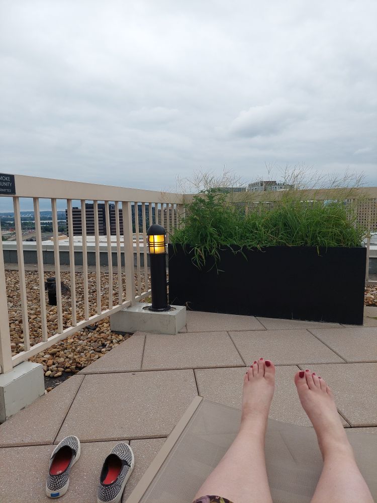 My legs on a deck chair on the roof of an apartment building. The sky is very gray and cloudy 