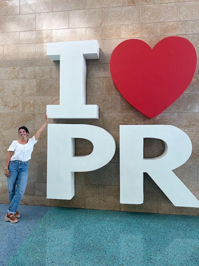 Elly is leaning against an "I Heart Puerto Rico" sign. 