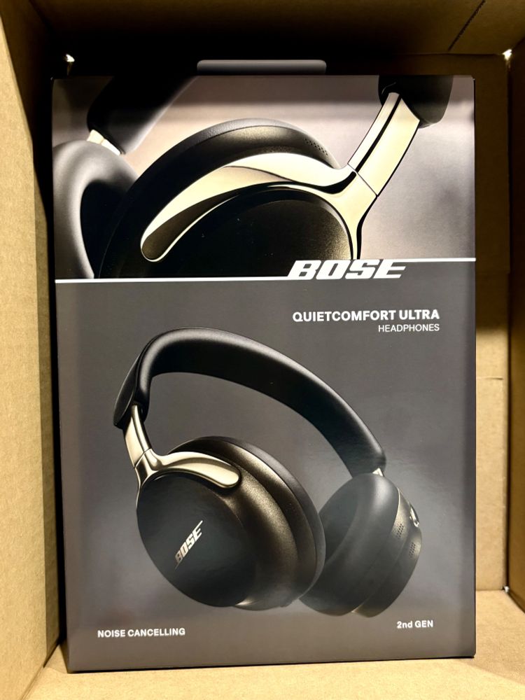 ボックスの中にある「Bose QuietComfort Ultra」のヘッドフォンのパッケージ。ヘッドフォンは黒色で、アームに金属のディテールがあり、「ノイズキャンセリング」と「2nd GEN」の文字が表示されている。