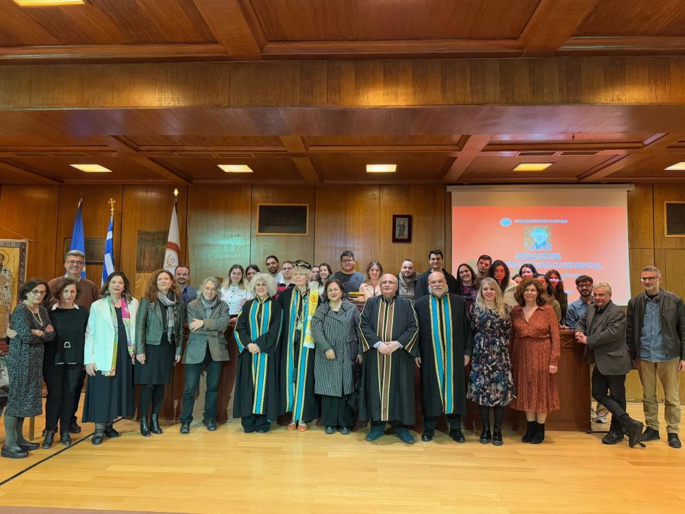 A group photograph of about thirty people. Those in the centre at the front wear academic dress. They stand in a modern wood paneled lecture theatre facing the camera and smiling.