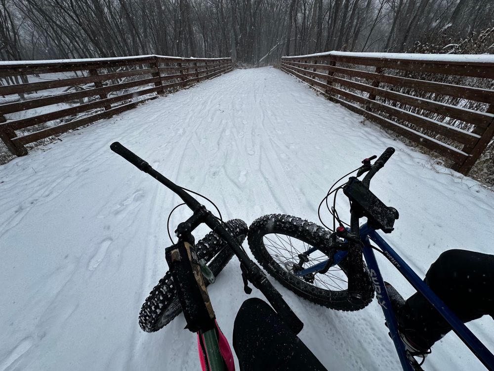 two fat bikes on a snowy bridge with their front wheels kissin