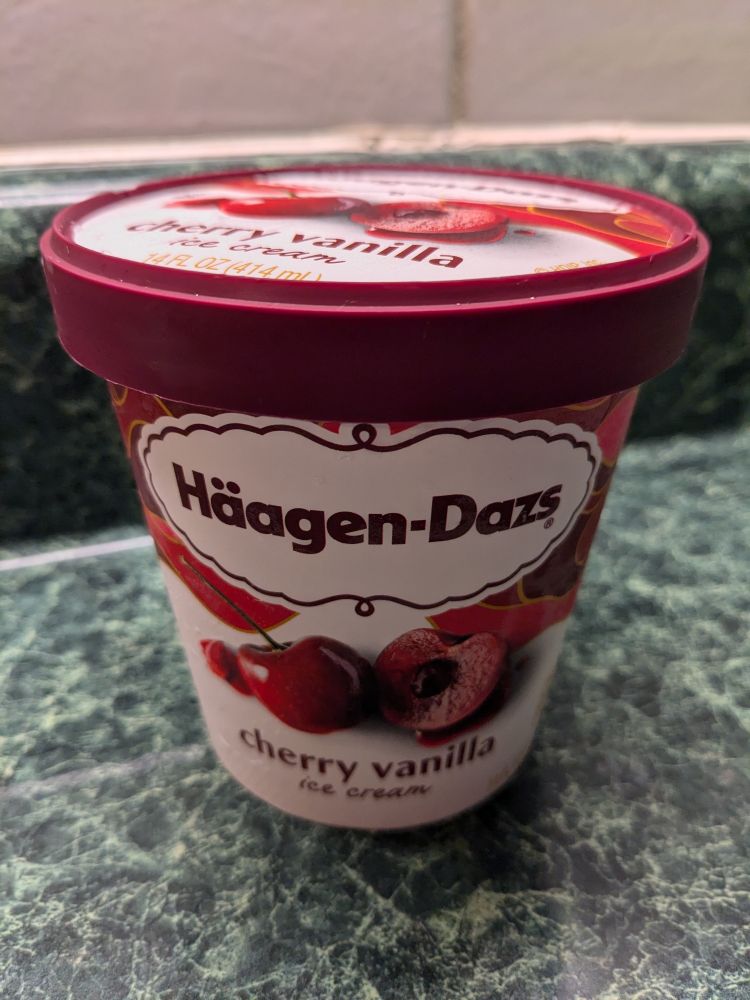 A pint of Hägen-Dasz cherry vanilla ice cream on a green kitchen counter.