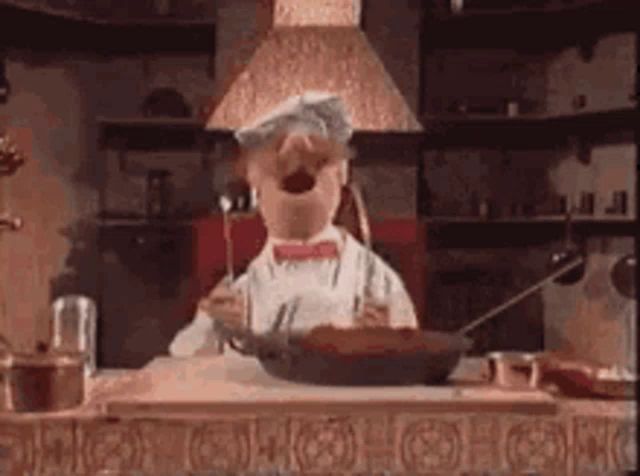 a muppet chef is standing in a kitchen with a frying pan in his hand .