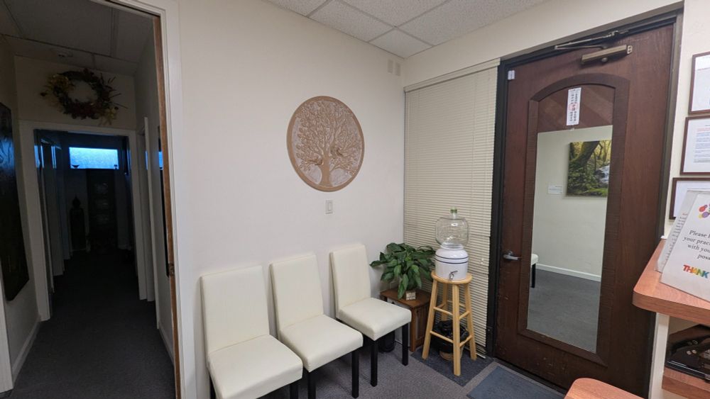 interior of waiting room area, three chairs, water urn, the door out on the right, and a hallway leading to treatment rooms on the left. 