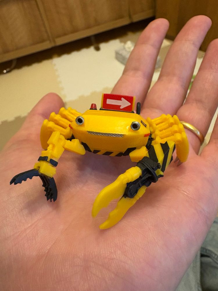 A photo of a capsule toy of a robotic crab with a yellow and black construction machinery colour scheme. 