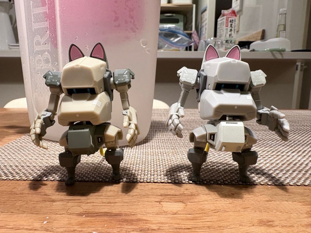 A photo of the same capsule toy stood next to another from the same series. The first one is a sandy colour, the second is grey. 
