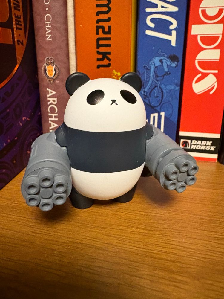 A photo of a capsule toy. The toy consists of a very cute, capsule-shaped panda bear with two mini guns for arms. I have no explanation for this fact. 