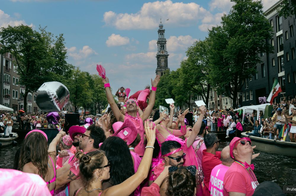 picture of me on the queer & sober boat on the canal of Amsterdam, everyone wearing pink, hands in the air enjoying myself very much